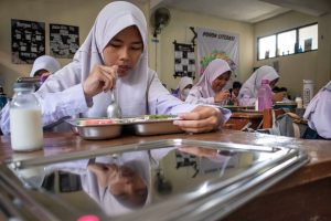 Remaja yang berinteraksi dengan ikon makanan sehat berwarna-warni dan perangkat, mewakili pendidikan nutrisi modern melalui media sosial.